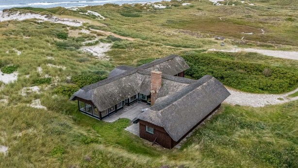 Ein Küstenhaus mit einem Reetdach, umgeben von Dünen und Grasland.