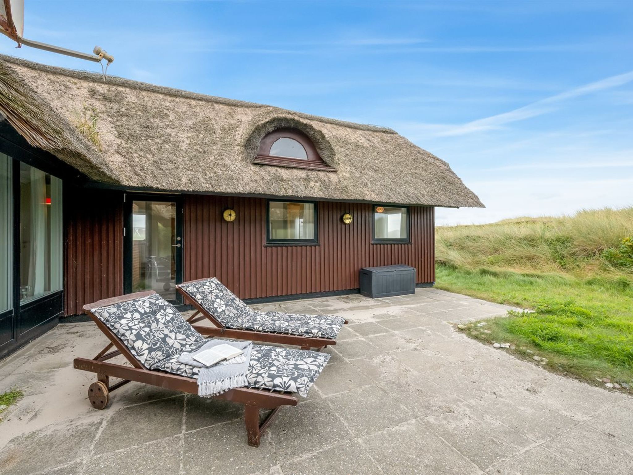 A thatched-roof building with two lounge chairs and a small window.