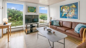 Ein Wohnzimmer mit braunem Ledersofa, einem Couchtisch, einem Fernseher und Kunstwerken an den Wänden.