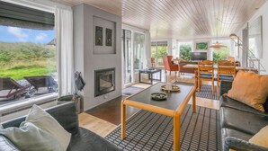 Ein geräumiges Wohnzimmer mit Kamin, großen Fenstern und Blick ins Freie.