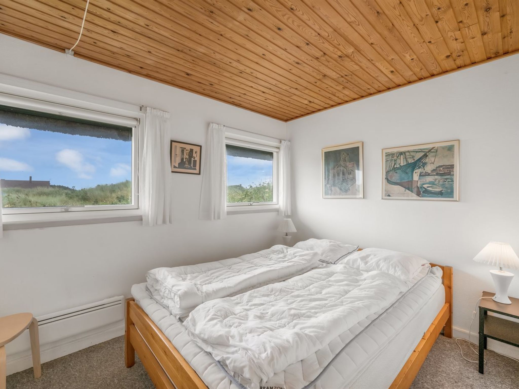 Une chambre à coucher avec un plafond en bois, deux lits, une table de chevet, une lampe et deux fenêtres avec des rideaux.