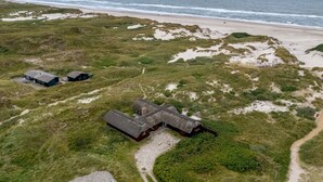 Eine Luftaufnahme einer Küstenlandschaft mit Strand, grasbewachsenen Dünen und mehreren Gebäuden.