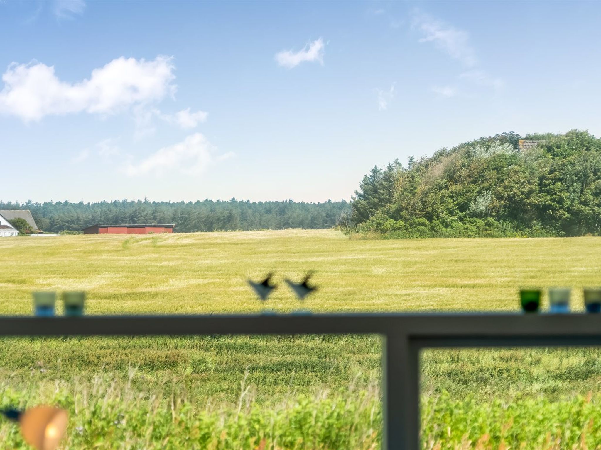 A rural landscape with a field, a red building, and a hill with trees.