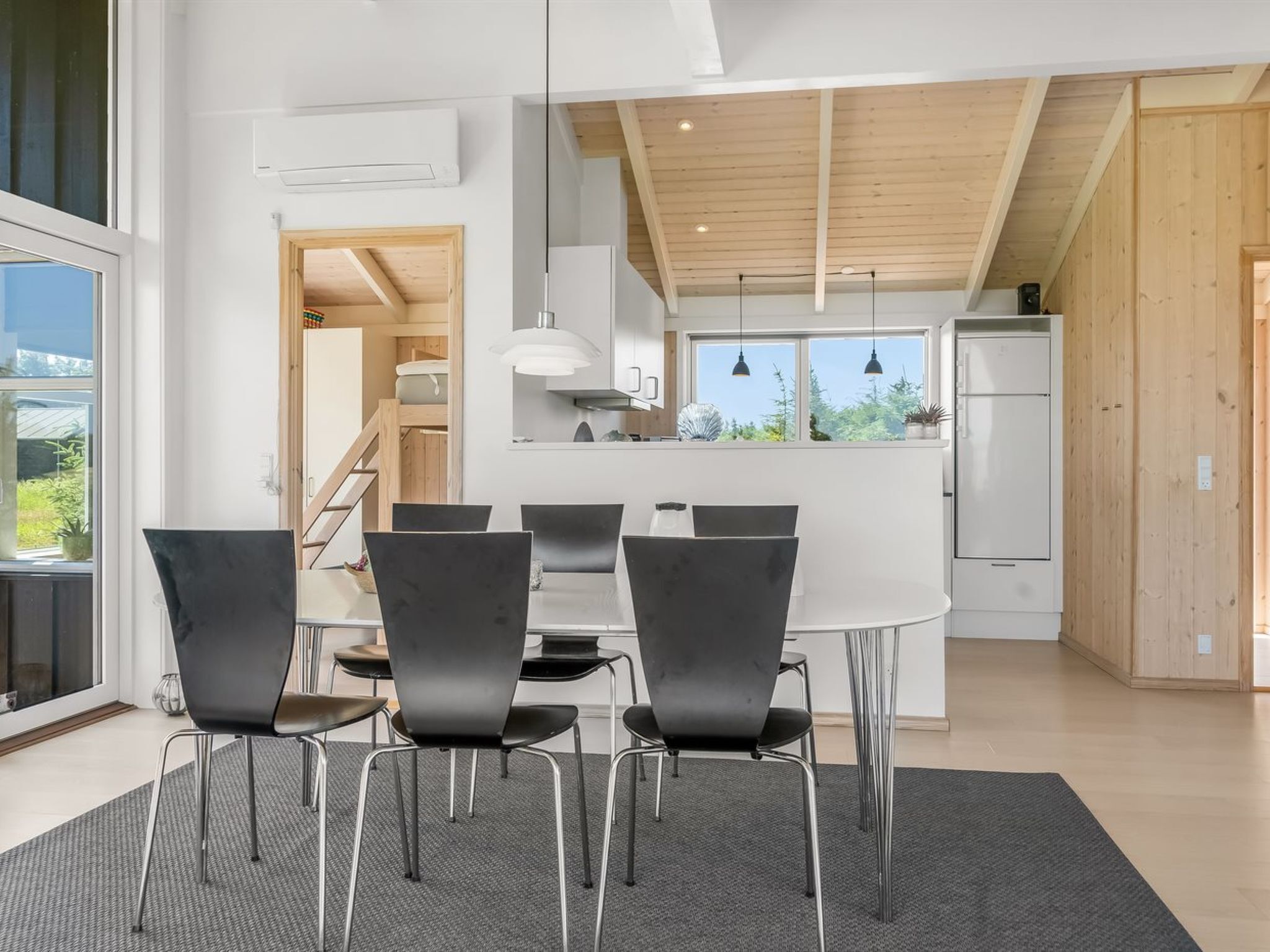 Une cuisine moderne dotée d’un îlot central, d’un coin repas avec une table ronde et des chaises, et offrant une vue sur l’extérieur grâce à de grandes fenêtres.