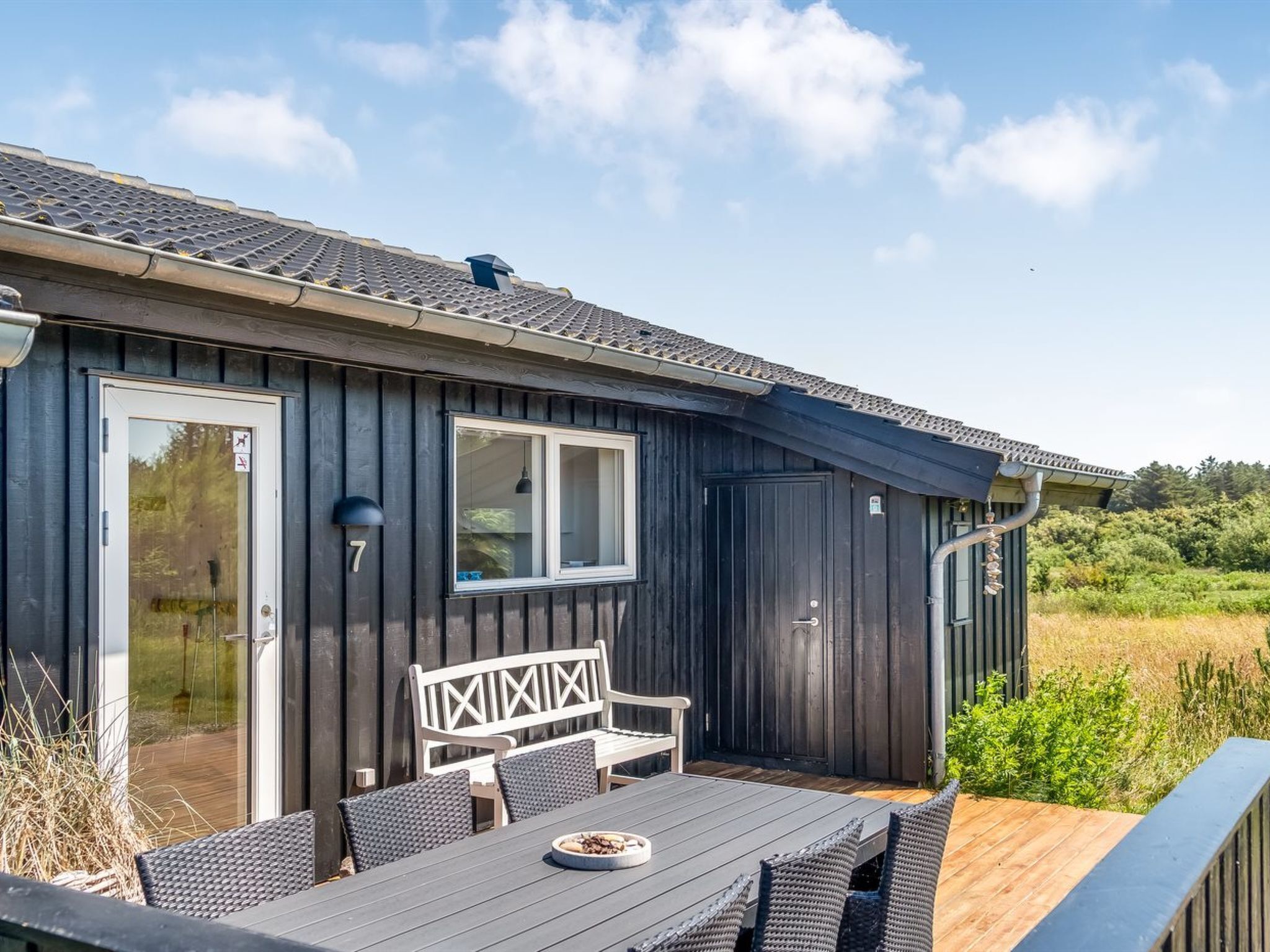 Een houten hutje met een terras, een bank en een tafel met buitenmeubels.