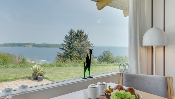 Una habitación con vista a un lago, una mesa con un frutero y una persona de pie junto a la ventana.