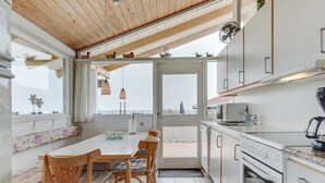 Una cocina moderna con armarios blancos, horno empotrado y comedor con mesa y sillas.