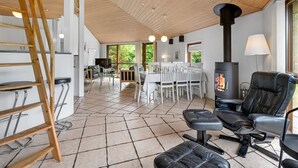 A spacious living area with a high ceiling, a fireplace, and a dining area with white chairs and a table. - "Reiner" - 300m to the fjord by Interhome (Skjern)