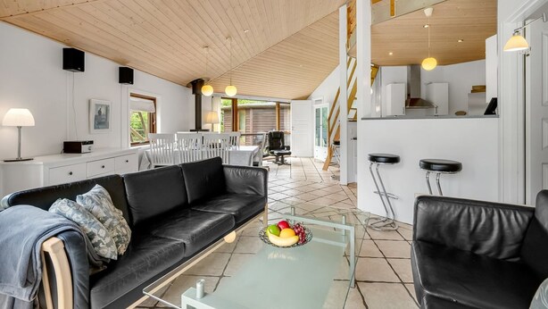 A modern living room with a black leather sofa, a glass coffee table with fruit, and a kitchen area with a bar and stools. - "Reiner" - 300m to the fjord by Interhome (Skjern)