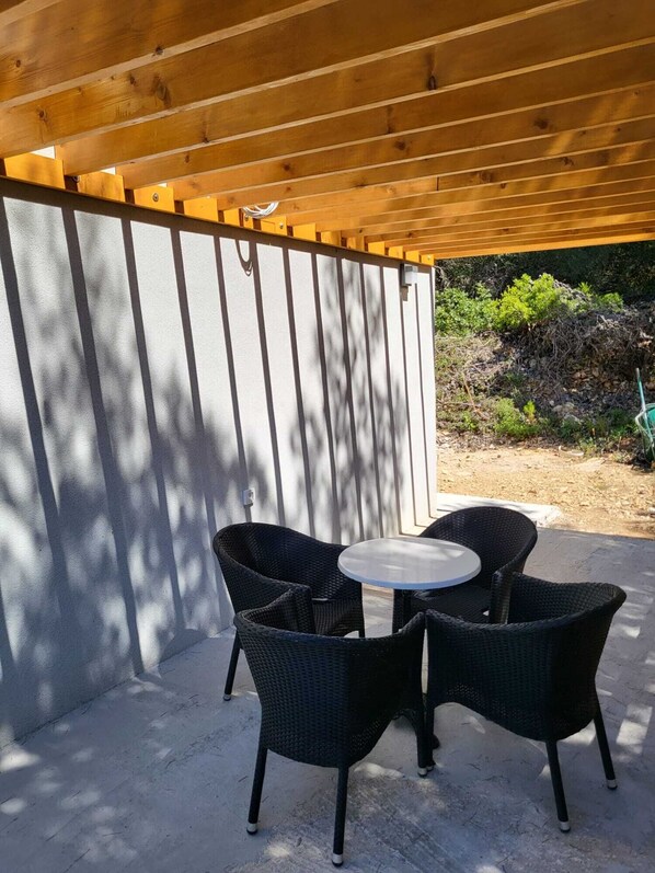 A covered patio area with a round table and four wicker chairs. - New vacation home with 2 terraces, right by the sea - a dream surrounded by forest (Murter)