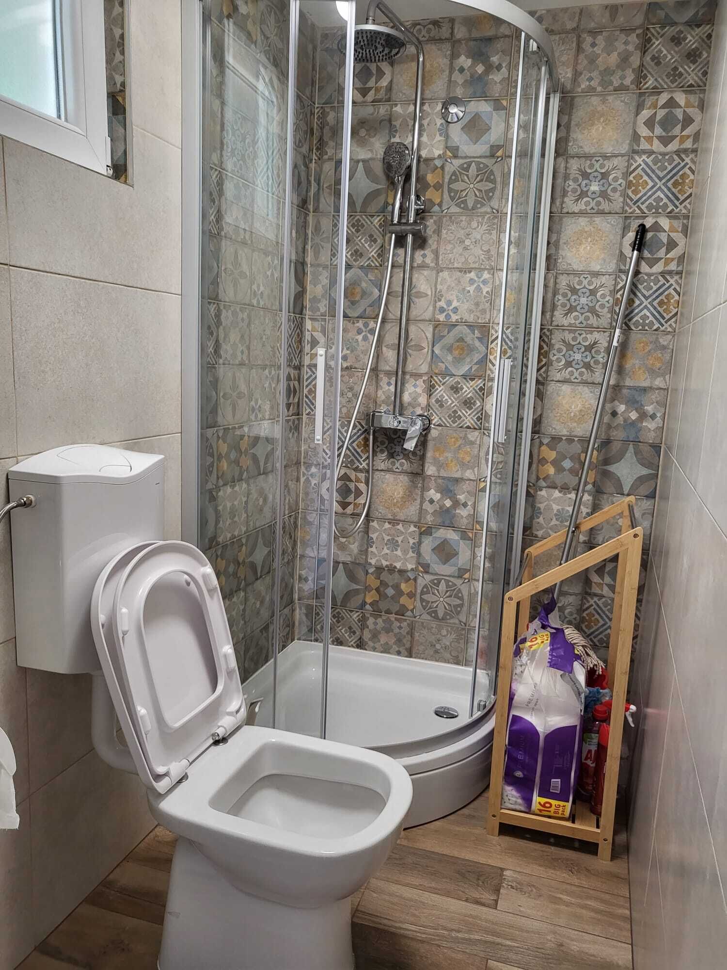 Ein Badezimmer mit Duschkabine, Toilette und Ablage für Reinigungsmittel.