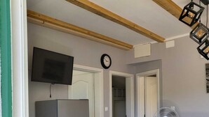 Una cocina funcional con refrigerador, una mesa de comedor con sillas, un televisor montado en la pared y un reloj.