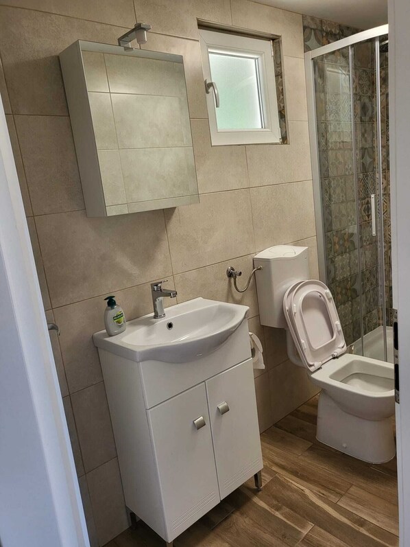 A bathroom with a sink, toilet, and shower area. - New vacation home with 2 terraces, right on the beach—a dream setting surrounded by forest (Murter)