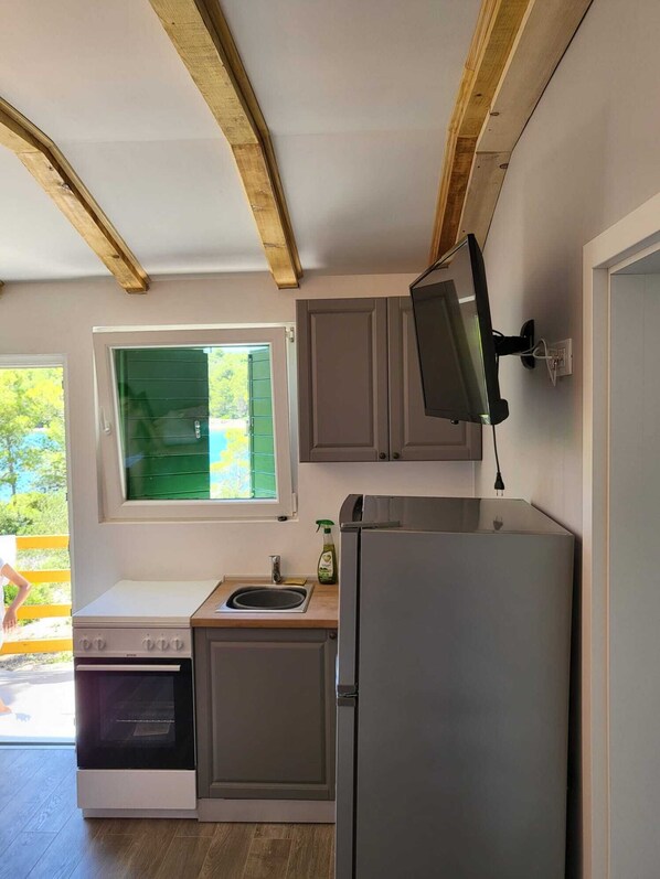 Cocina compacta con horno empotrado, lavamanos y refrigerador. Se ve un ventanal con vistas a zonas verdes.
