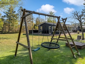 A wooden swing set with a tire swing in a grassy yard with a house in the background.