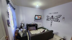 Ein Wohnzimmer mit einem dunklen Sofa, einem an der Wand befestigten Fernseher und einer Wanddekoration mit einem Libellenmotiv.