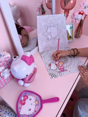 A Hello Kitty-themed coloring book on a pink table with a Hello Kitty figurine and a Hello Kitty mirror.