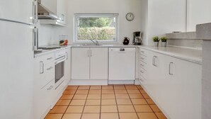 A modern kitchen with white cabinets, a wooden ceiling, a window with blinds, a clock, and a coffee maker.