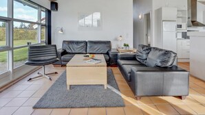 A modern living room with a leather sofa, a wooden coffee table, and a large window offering a view of the outdoors.