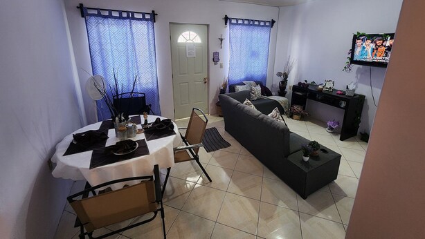 Una sala de estar con un sofá, una mesa de comedor con sillas, un televisor y una puerta con ventanal.
