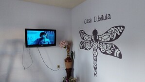 Una habitación con televisor montado, un diseño de libélula en la pared y un jarrón con flores.