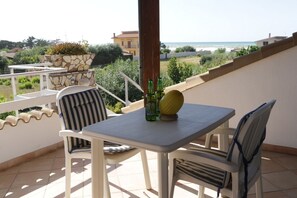 A balcony with a table and chairs, a potted plant, and a view of the sea.