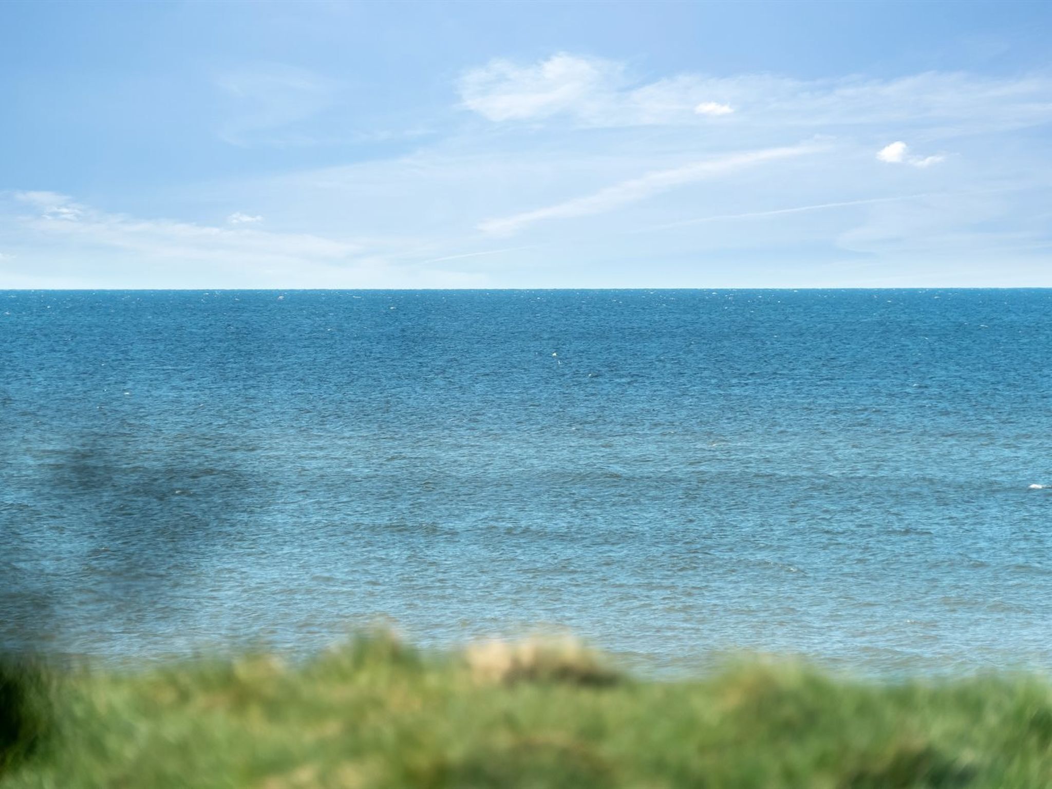 Blick auf das Meer bei klarem Himmel und vereinzelten Wolken.