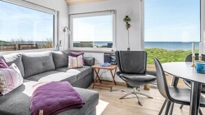 A modern living room with a grey sofa, a black chair, and a small table. Large windows offer a view of the sea. - "Trifun" - 50m from the sea by Interhome (Løkken)