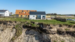 A modern house with a grey roof and white walls, situated on a grassy area with a rocky foreground. - "Trifun" - 50m from the sea by Interhome (Løkken)