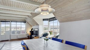 Tilava ruokailutila, jossa on pitkä pöytä, sinisellä kankaalla verhoillut tuolit ja moderni kattovalaisin.