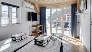 Huoneessa on puinen katto, televisio, patjallinen sänky, pieni pöytä ja ikkuna.