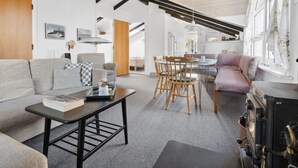 A modern interior with a high ceiling, exposed beams, a dining area, and a cozy seating space.