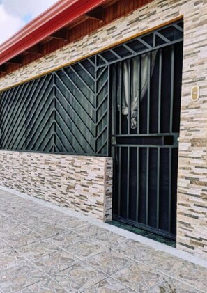 Fachada de edifício com exterior em pedra, telhado vermelho e janela com padrão de grade metálica.