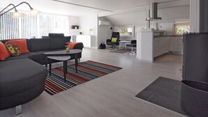 Ein modernes Wohnzimmer mit einer Couch, einem Couchtisch und einem Essbereich mit Stühlen. Es gibt eine Küchenzeile mit Schränken und einem Kühlschrank.