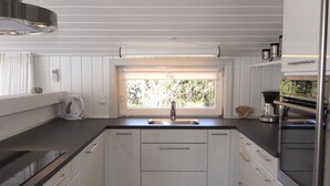 Eine moderne Küche mit weißen Schränken, einer Spüle aus Edelstahl und einem Fenster mit Jalousien.