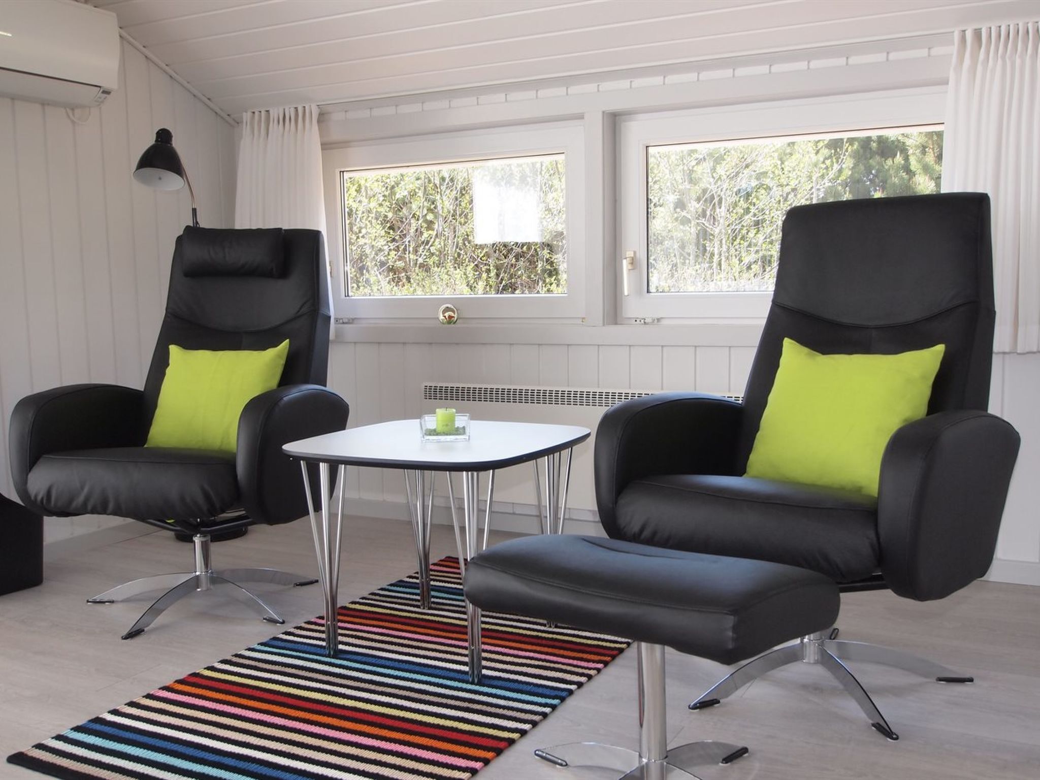 A modern room with two black leather chairs with neon green cushions, a small round table with a candle, and a colorful striped rug.