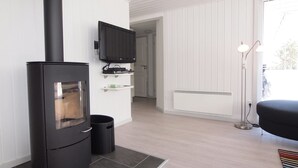 Ein modernes Wohnzimmer mit einem schwarzen Kaminofen, einem flachbildfernseher an der Wand und einem großen Fenster, das für natürliches Licht sorgt.