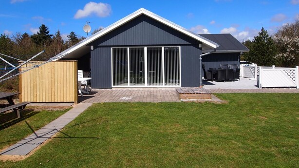 Ein modernes Haus mit großen Schiebegläsern, einer Terrassenfläche und einem umzäunten Garten.