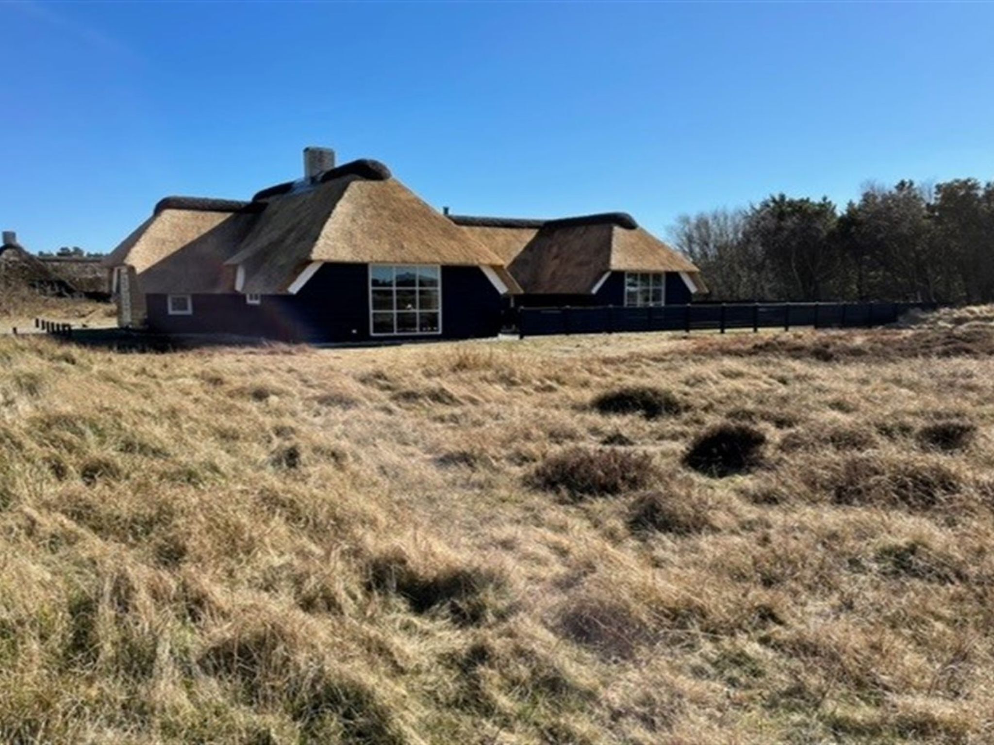 A house with a thatched roof and a stone chimney, surrounded by dry grassland and trees.