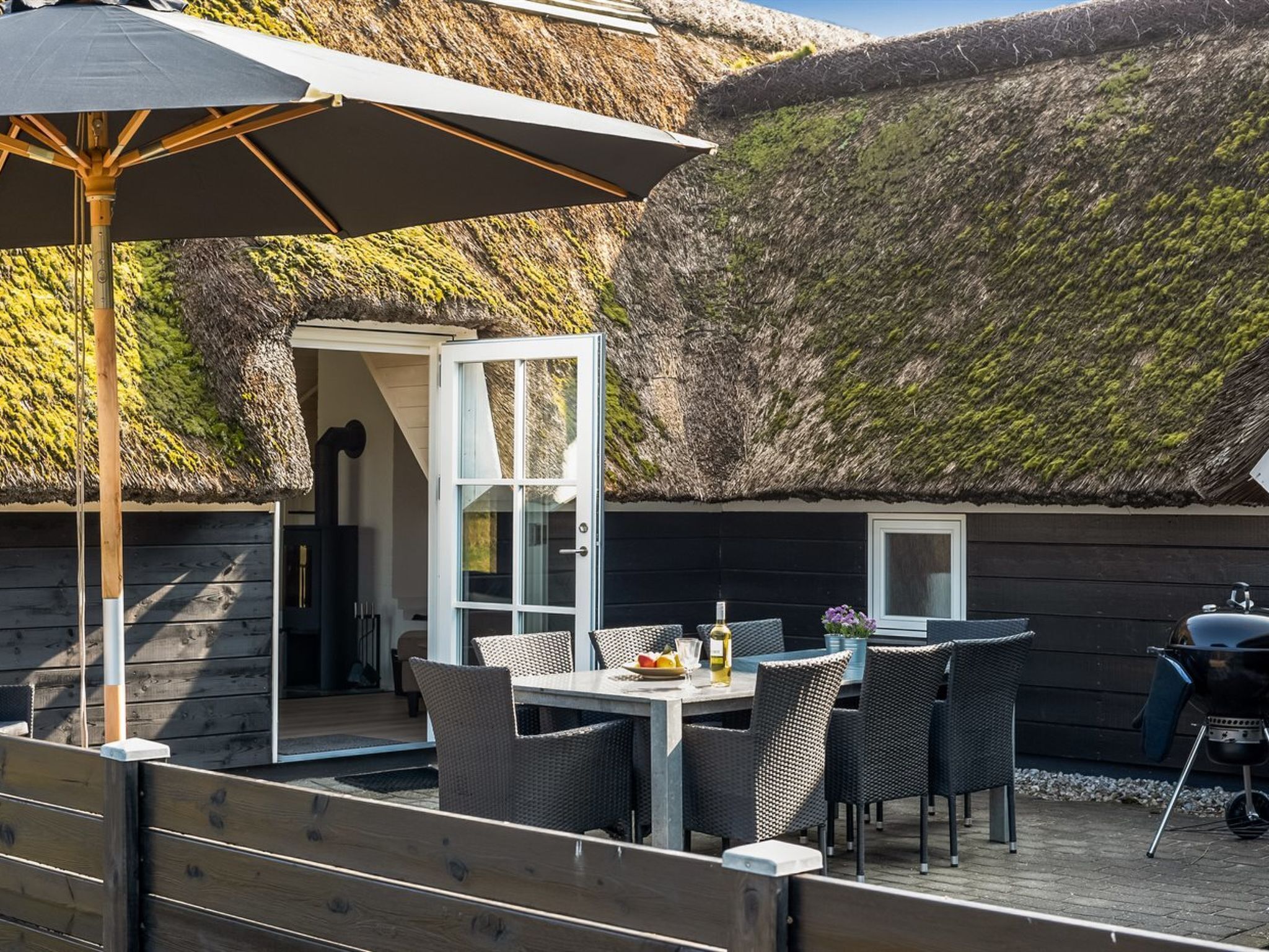 An outdoor dining area with a table and chairs, a grill, and a thatched roof structure.