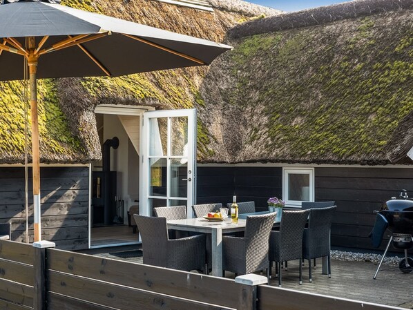 An outdoor dining area with a table and chairs, a grill, and a thatched roof structure.