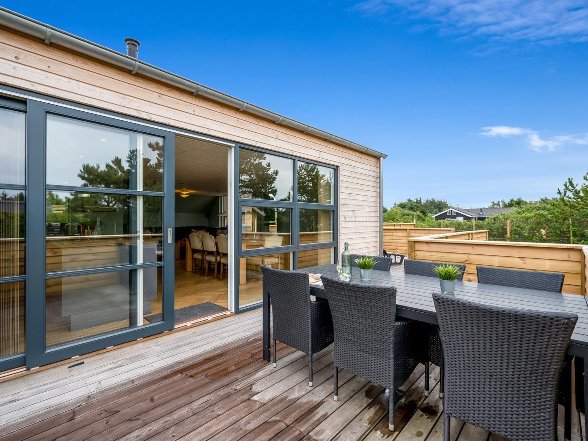 A modern house with a deck, large sliding glass doors, and outdoor furniture.