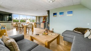 Een ruime woonkamer met een eettafel, banken en een keuken met een fornuis.