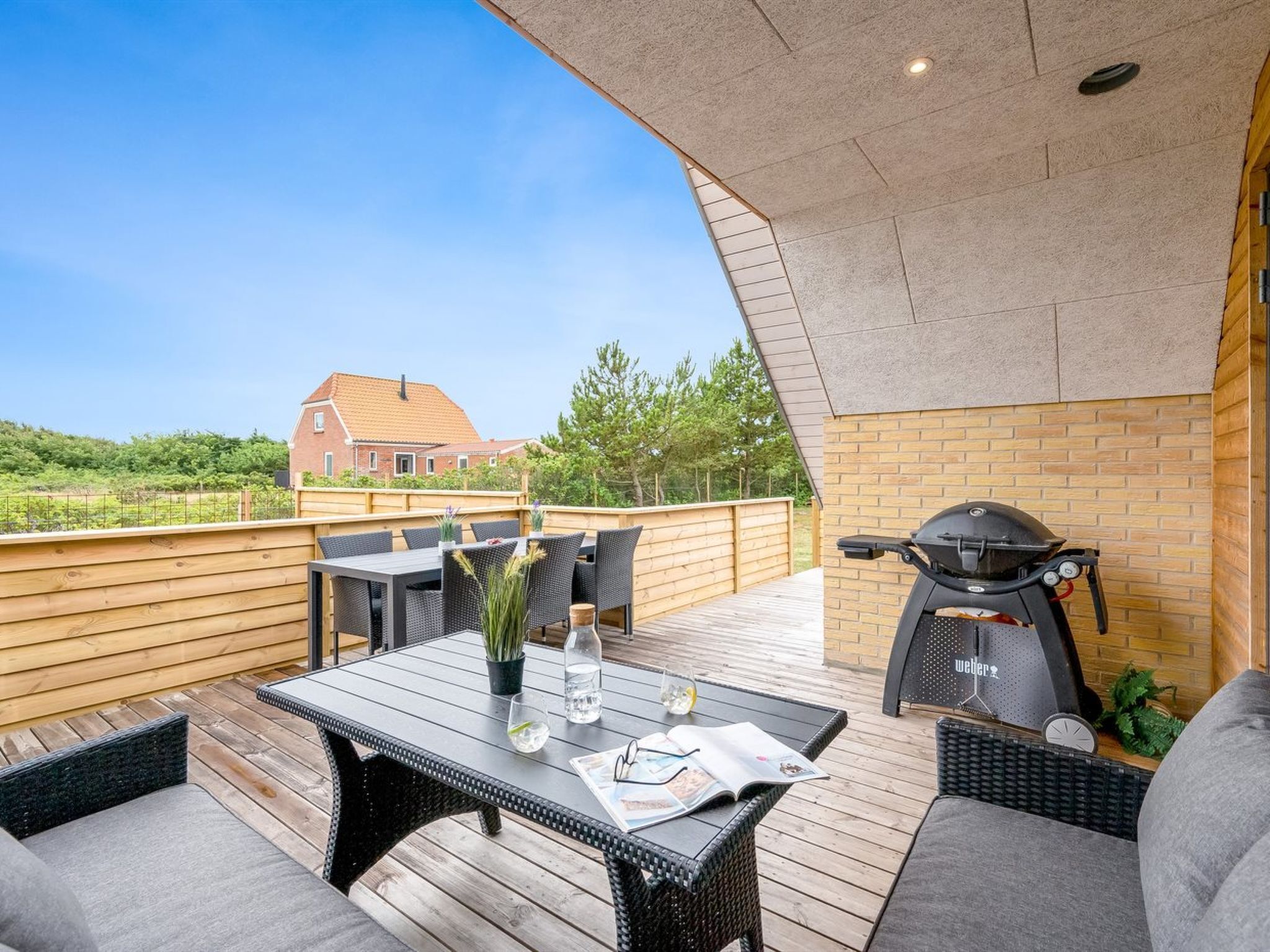 An outdoor patio with a table, chairs, a grill, and a view of a house in the background.