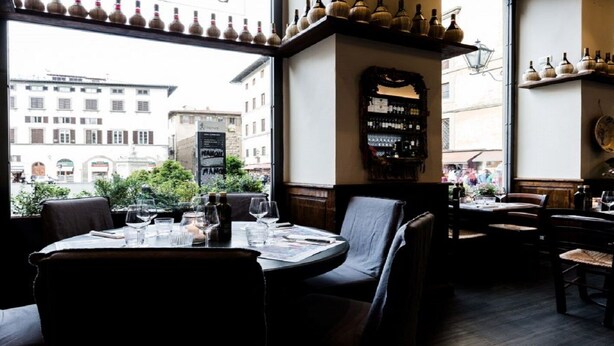 Un restaurante con mesas listas para comer, un cartel con el menú y vista a la calle.