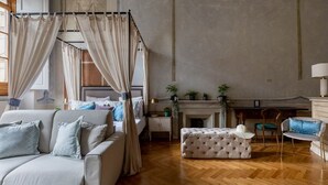 Un dormitorio con cama con dosel, un sofá, un reposapiés capitonado, una chimenea y un escritorio con lámpara.