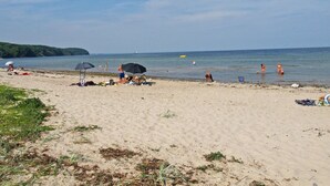 Ein Strand mit badenden Personen, Sonnenschirmen und blauem Himmel.