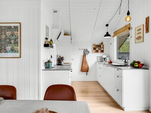 A modern kitchen with white cabinetry, a dining area with a table and chairs, and a hanging light fixture.