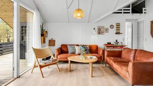 A spacious living area with a large window, a wooden floor, a brown leather sofa, a wooden coffee table, and a hanging light fixture. - "Ilsi" - 1.5km from the sea by Interhome (Blåvand)