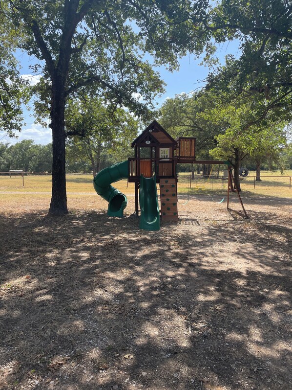 A playground with a slide and climbing structures, surrounded by trees and open space.